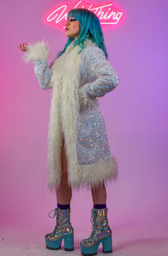 A female model with blue hair wearing a sparkly Afghan coat and silver platform heeled boots