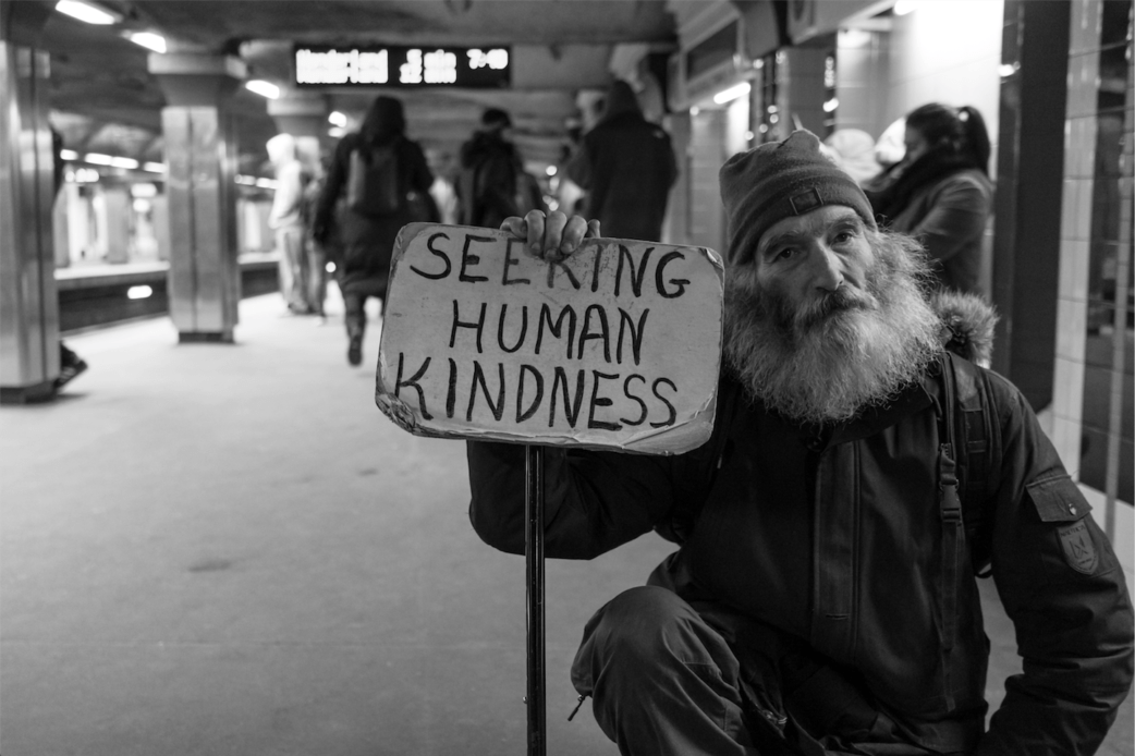 Photo of Homeless man holding a sign that says "Seeking Human Kindness"